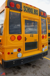 Rear view of a yellow 2019 Ford Blue Bird E-Series school bus showing 'SCHOOL BUS' sign, brake lights, and emergency door label on the back.