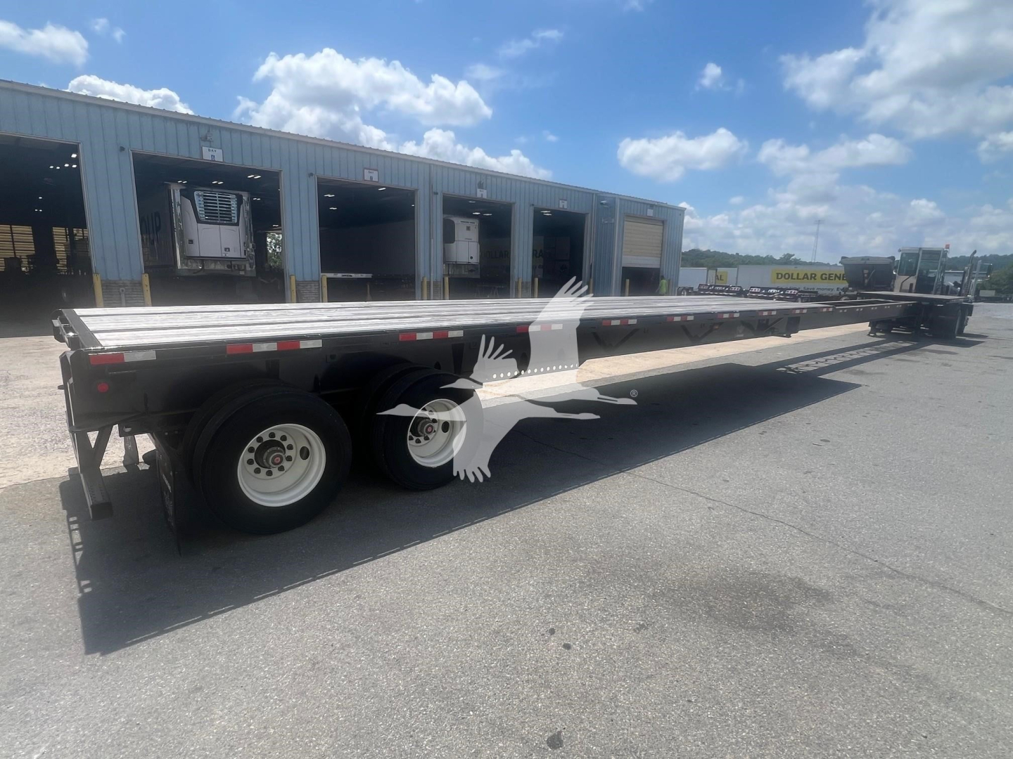 Manac air ride extendable flatbed trailer side view showing tandem axles and long flatbed with reflective tape