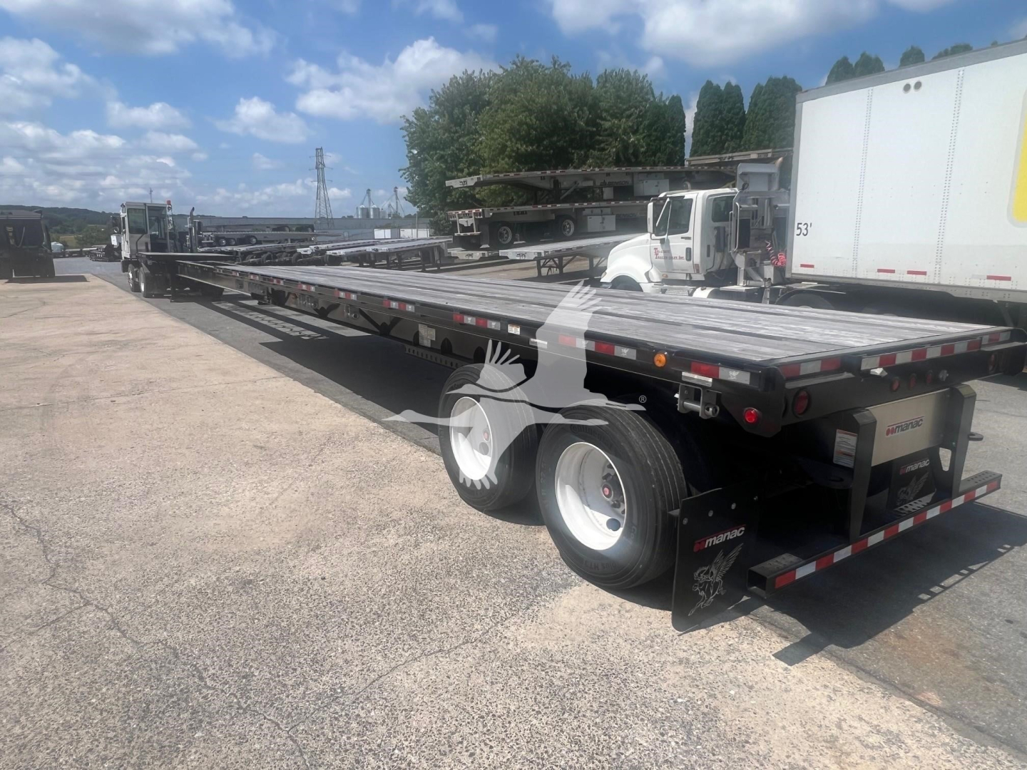 Manac air ride extendable flatbed trailer in a parking lot, rear view showing dual rear axles and reflective safety tape.