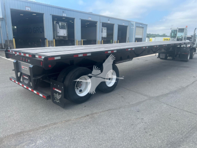 Manac air ride extendable flatbed trailer shown from the rear side, dual rear axles, long steel deck with reflective tape and tail lights.