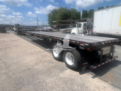 Manac air ride extendable flatbed trailer in a parking lot, rear view showing dual rear axles and reflective safety tape.