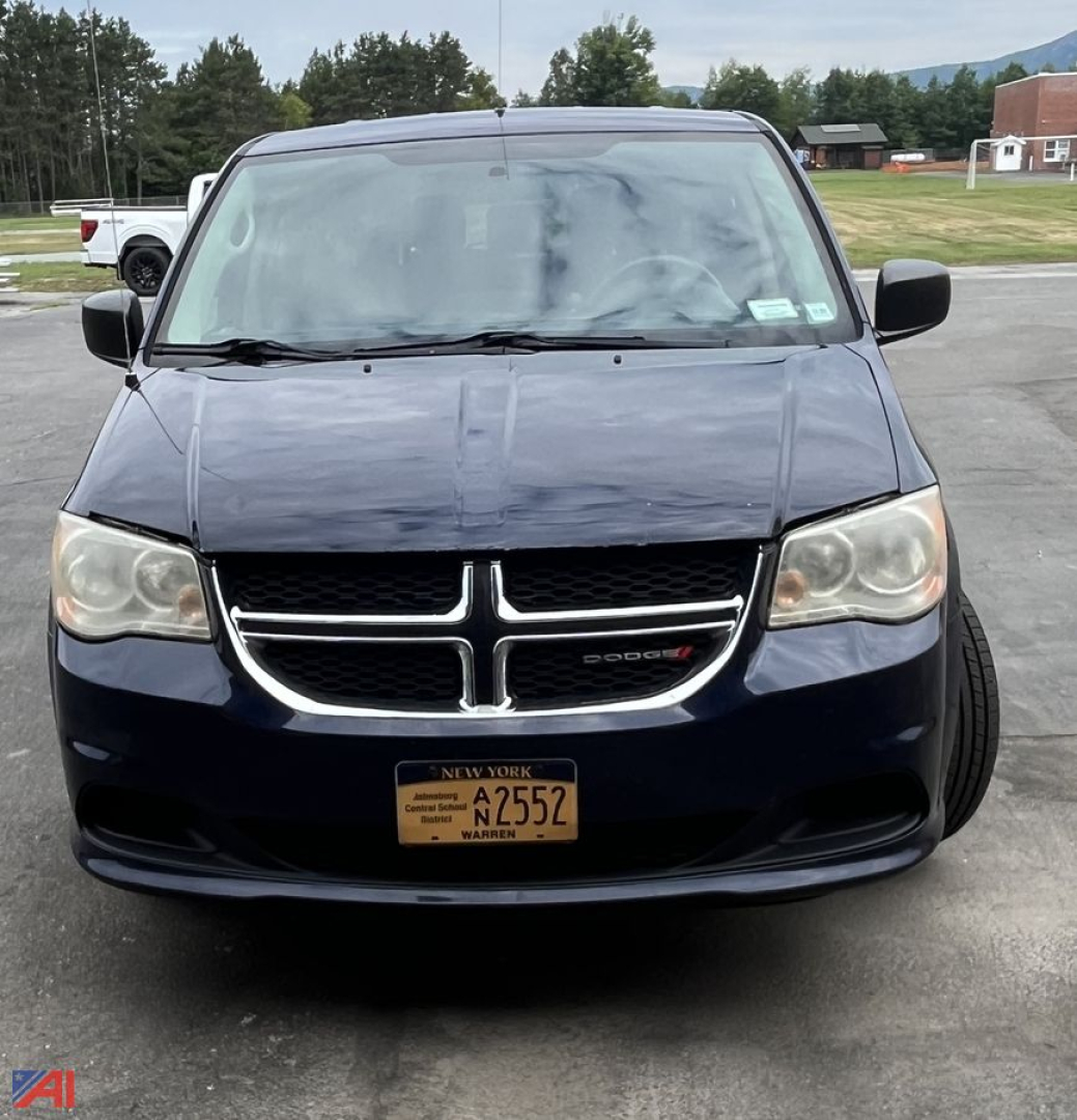 Front view of a dark blue 2013 Dodge Grand Caravan with NY license plate A2552, grille emblem visible, headlights, and windshield wipers.