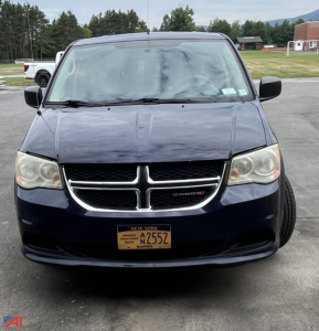 Front view of a dark blue 2013 Dodge Grand Caravan with NY license plate A2552, grille emblem visible, headlights, and windshield wipers.