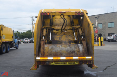 Rear view of a yellow Mack Granite dump truck with tailgate and warning label, in-service condition.