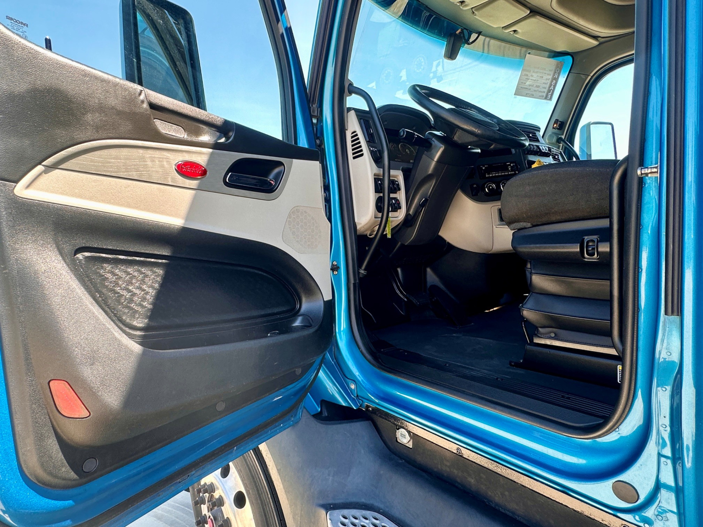 Truck cab interior of a 2022 Peterbilt 579 showing front door open, steering wheel, dashboard, and driver seat.