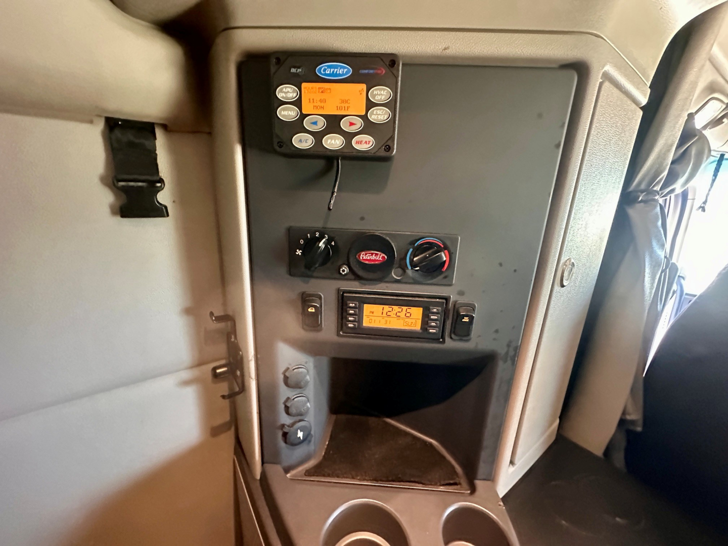 Truck dashboard panels showing Carrier command control unit, climate controls, and a small display with text; lower compartment and two cup holders visible.