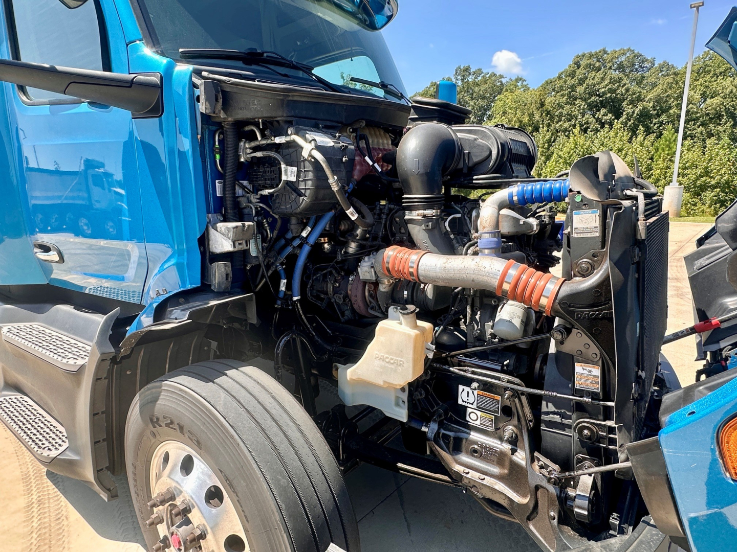 Peterbilt 579 engine bay showing exposed components and hoses. Blue cab, radiator and intercooler visible with hoses and wiring.