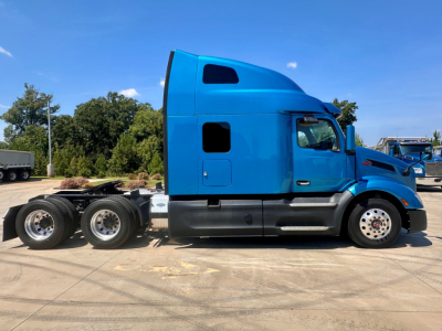 Side view of a blue 2022 Peterbilt 579 semi-truck tractor tractor cab with sleeper, showing two rear axles and chrome wheel rims.