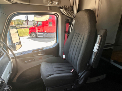 Peterbilt 579 cab interior showing driver seat and door panel. View through the open window reveals a red truck outside.