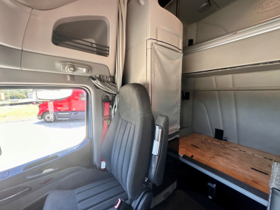 Peterbilt 579 sleeper cab interior showing driver seat and cargo area; side window and overhead storage in view.