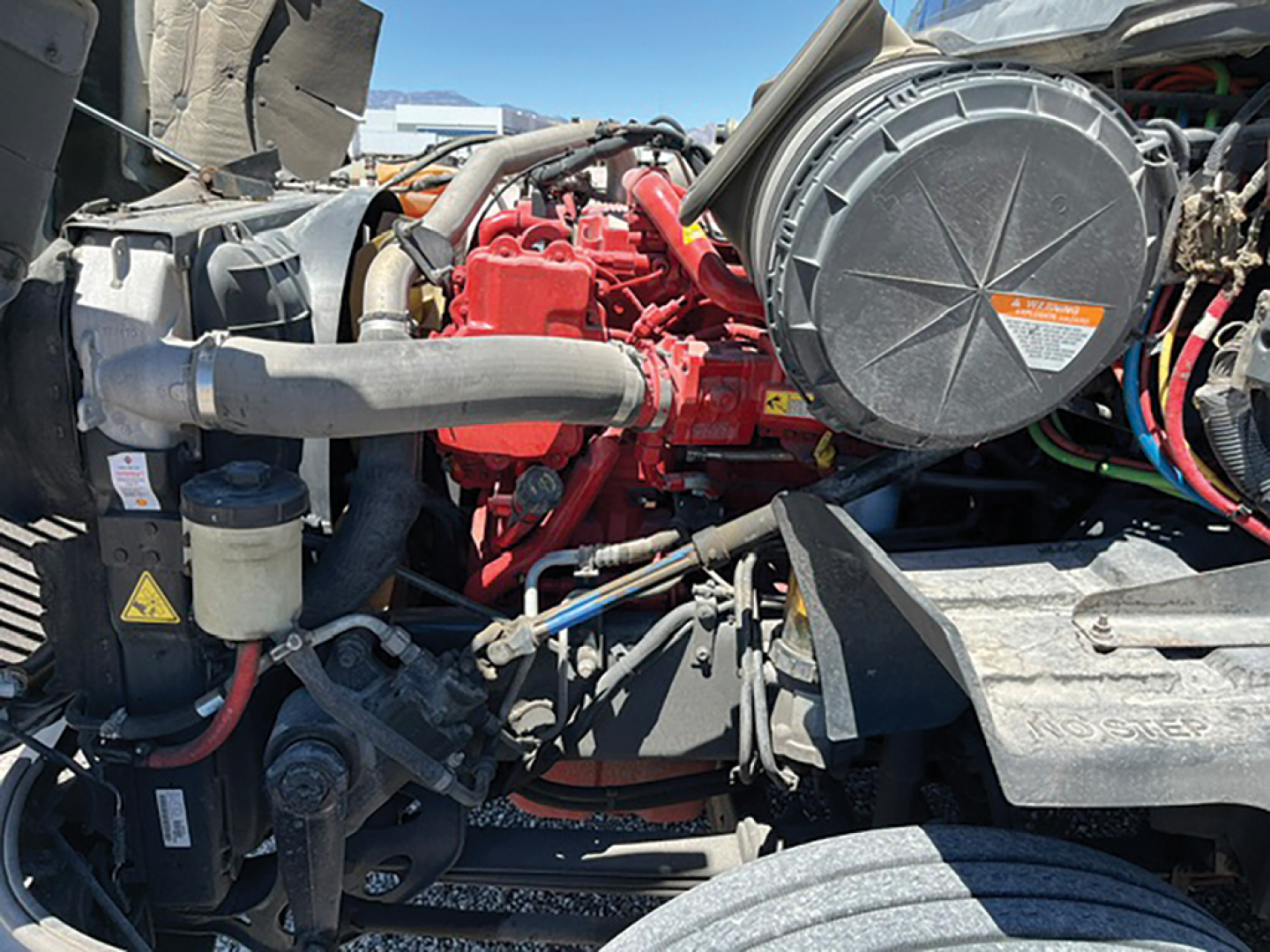 Truck engine bay showing red engine, large black air intake housing, hoses, wiring, and metal components.