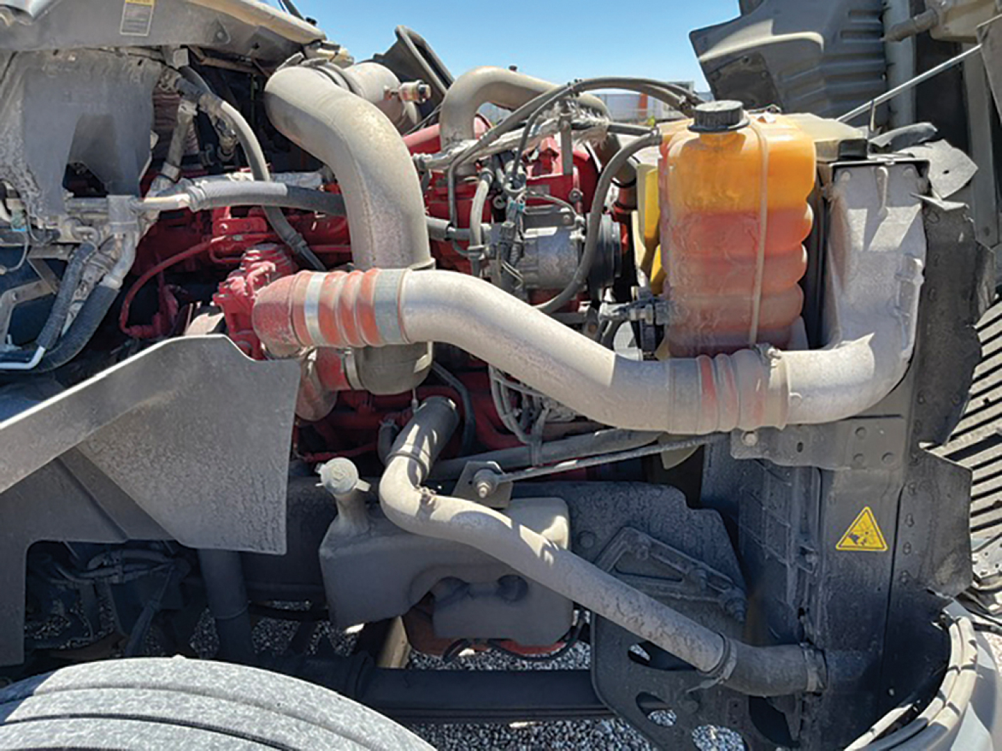 Truck engine bay showing diesel engine and cooling system components with orange coolant reservoir and various hoses.
