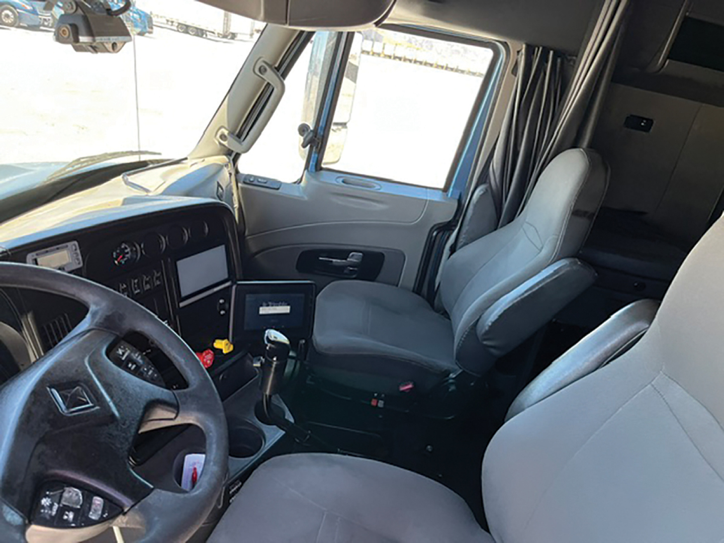 Interior of a 2015 International ProStar122 sleeper truck cabin showing steering wheel, instrument cluster, driver and passenger seats, center console, and gear shifter.