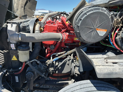 Truck engine bay showing red engine, large black air intake housing, hoses, wiring, and metal components.