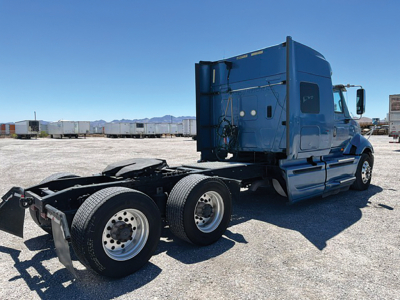Blue 2015 International ProStar122 tractor rear three-quarter view showing tandem rear axles and sleeper cab. Visible components include fuel tanks, side steps, and exhaust stack.