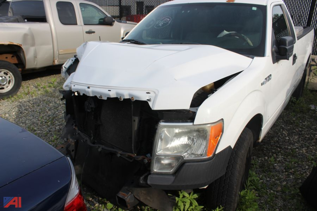 Front view of a white 2012 Ford F-150 with front-end damage; hood misaligned, exposed radiator area, headlight and bumper assembly missing and debris in grille opening.