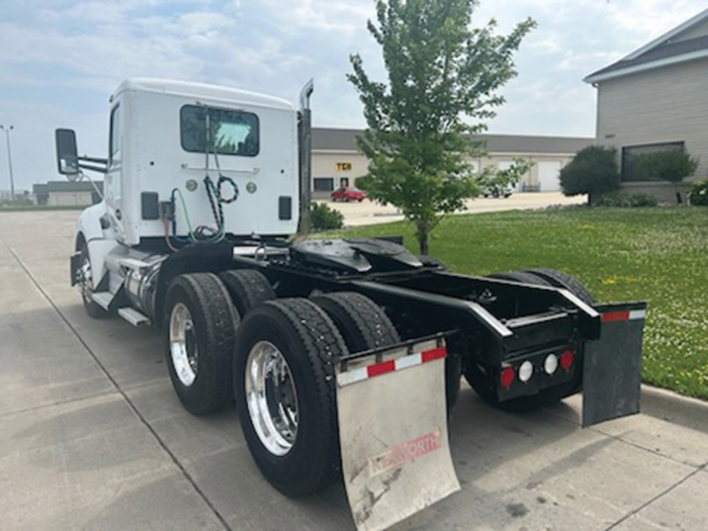 Kenworth T680 tractor in-service with sixth-wheel configuration showing rear view, dual rear axles, white cab, aluminum wheels, and mud flaps.