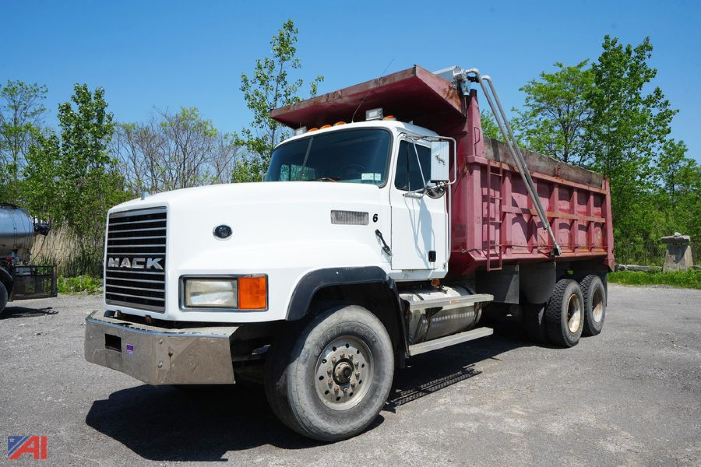 Dump truck showing Mack CL713 front grille and white cab with red dump body, side view, with hydraulic lift mechanism.