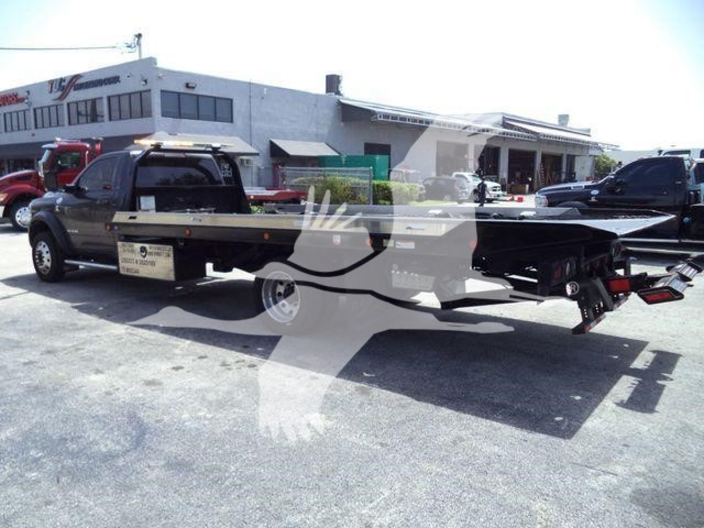 Ram 5500 rollback truck in a dealership lot with a long flatbed and rear equipment visible.