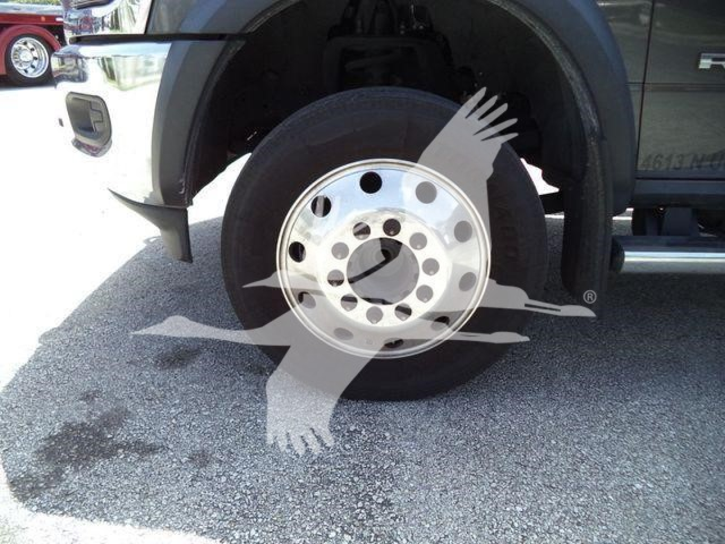 Ram 5500 front wheel and fender view showing alloy hub and tire, part of a rollout/heavy-duty truck in a dealership lot.