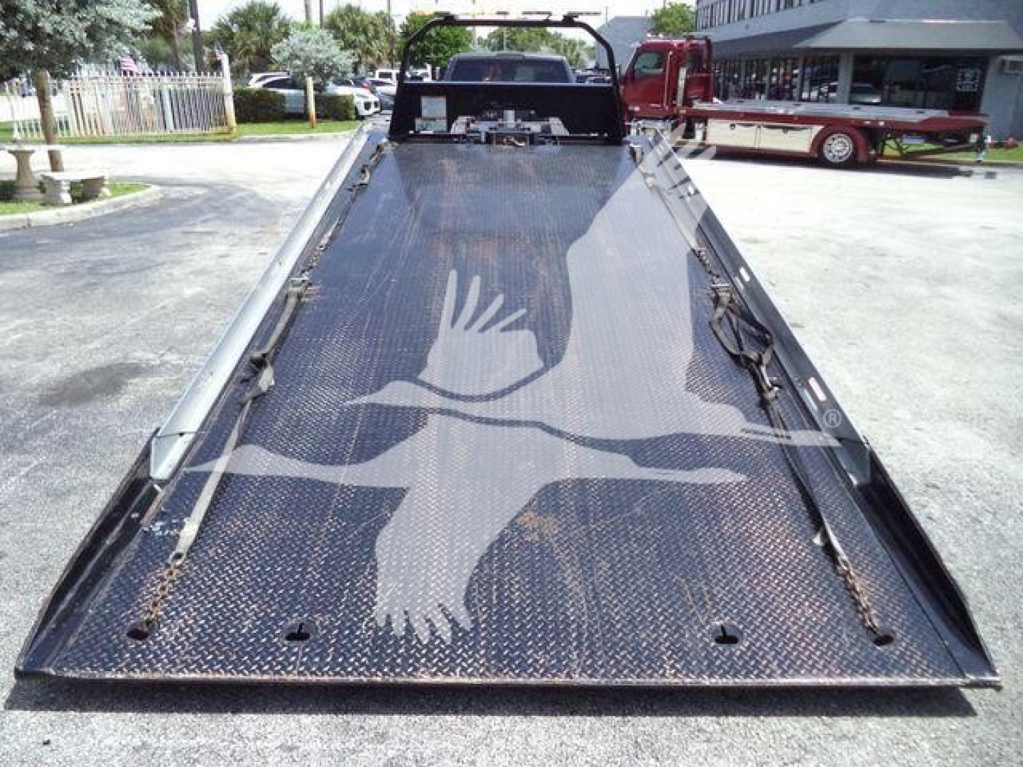 Ram 5500 rollback truck flatbed with black diamond plate surface and bird graphic on bed, rear view showing loading ramp.