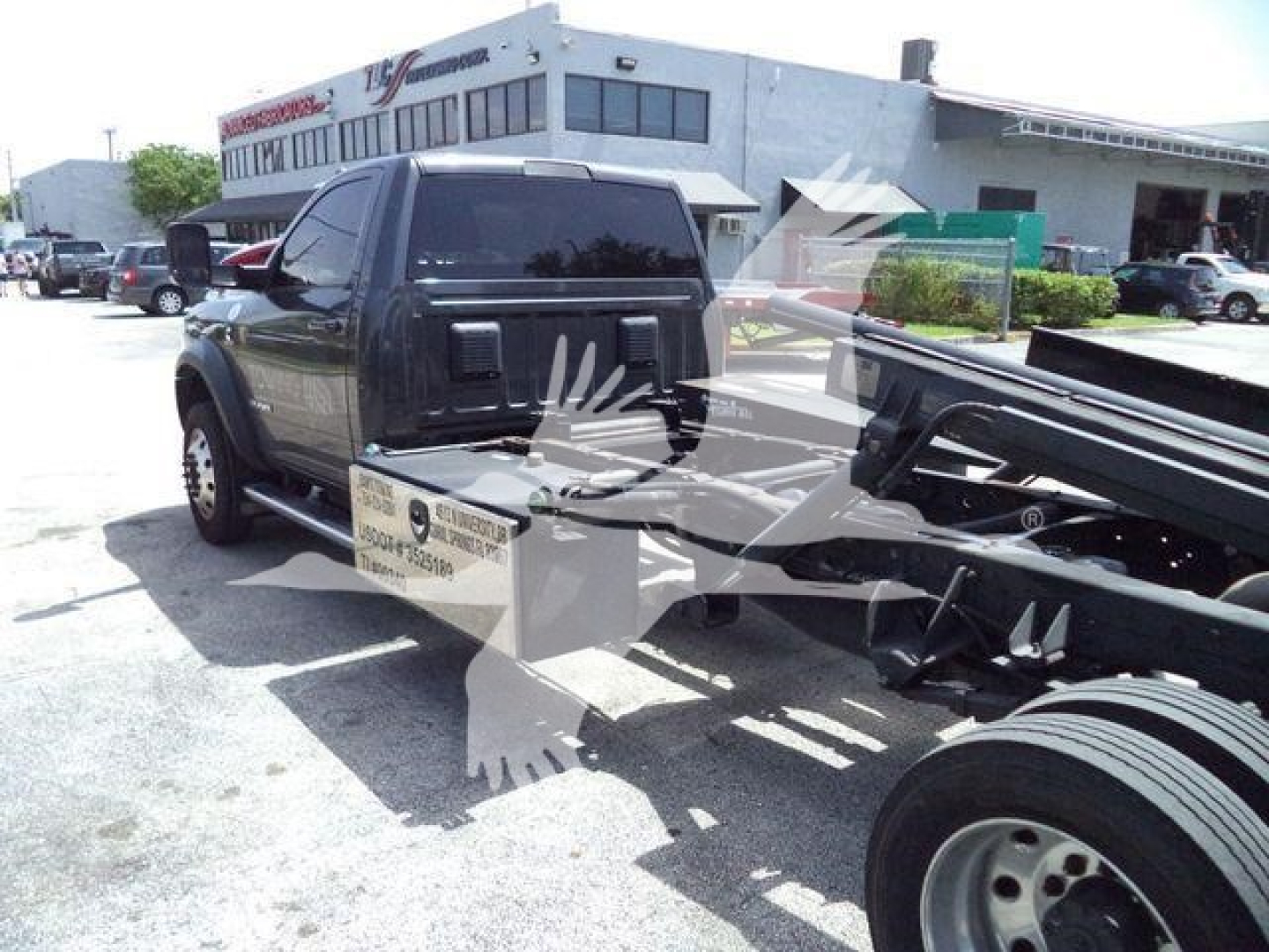 Ram pickup truck in a dealership lot with rollback tow bed attached; visible text includes stock number plate and building signage in background.