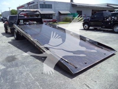 Ram 5500 rollback flatbed truck in-service showing long steel ramp bed and rear extension with hydraulic system and toolbox area.