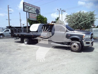 Ram 5500 rollback truck in a lot showing a flatbed with a tank and crane, side view; no legible small text identifiable on components.