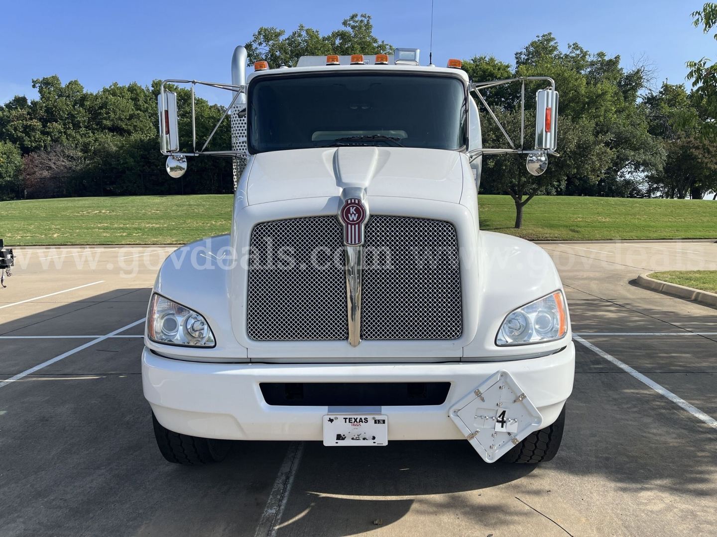 Front view of a white Kenworth T370 service truck showing grille with Kenworth emblem, large headlights, side mirrors, and a diamond plate hazard plate on the bumper area.