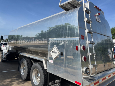 Kenworth T370 service/utility truck in service with polished aluminum tank and rear access ladder. Visible diamond placard, taillights, bumper, and rear doors.