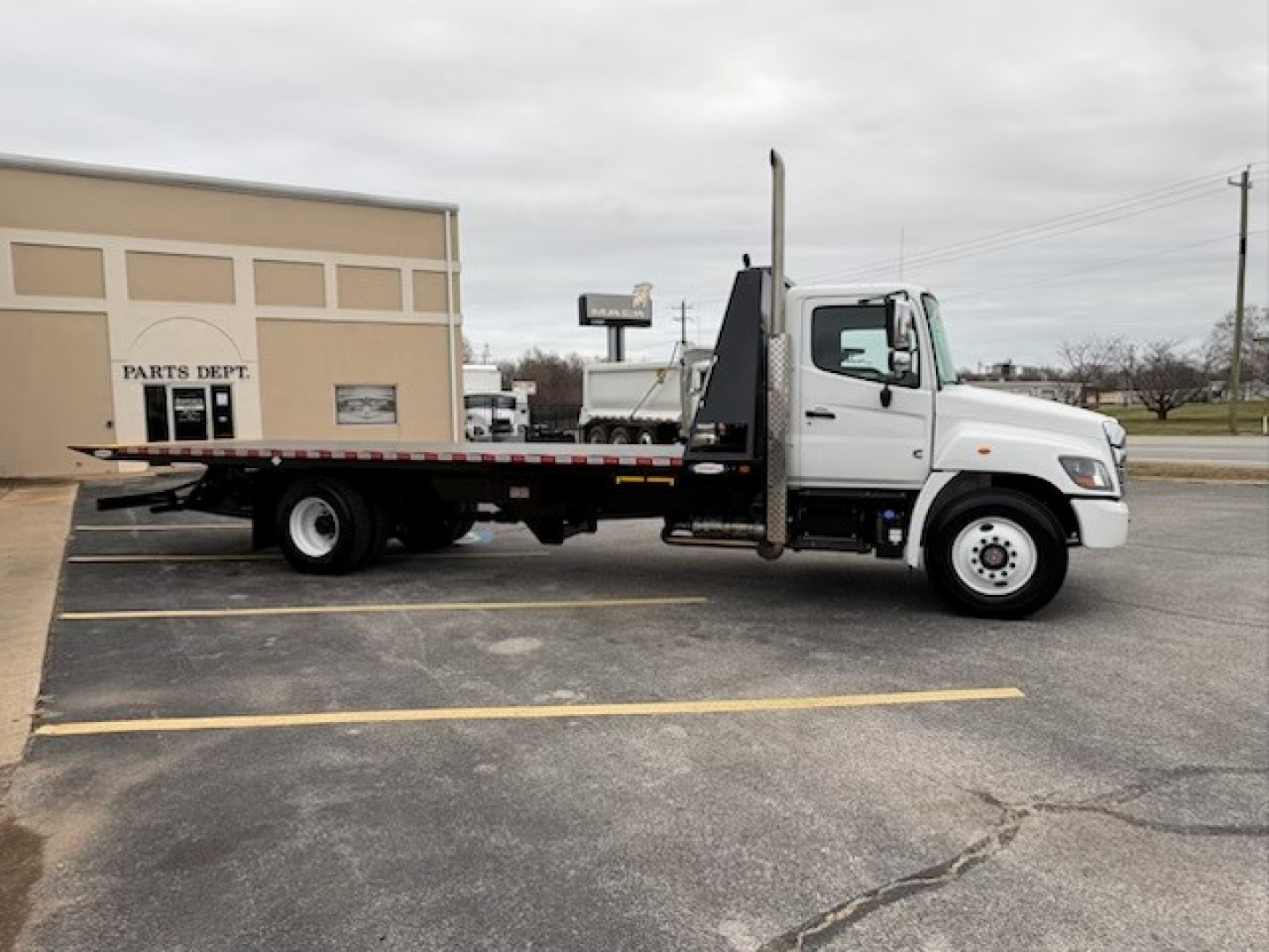 Flatbed tow truck side view showing white cab and long dark platform with hydraulic lift in a parking lot.