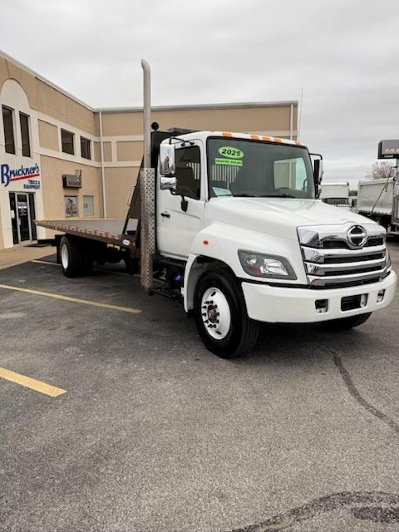 2025 Hino L7 rollback truck in white with tow/rollback bed and vertical exhaust stack, front three-quarter view.