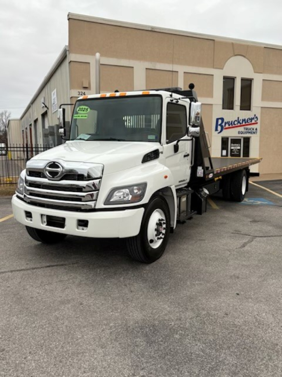 White 2025 Hino L7 rollback truck parked in lot showing front grille and flatbed.