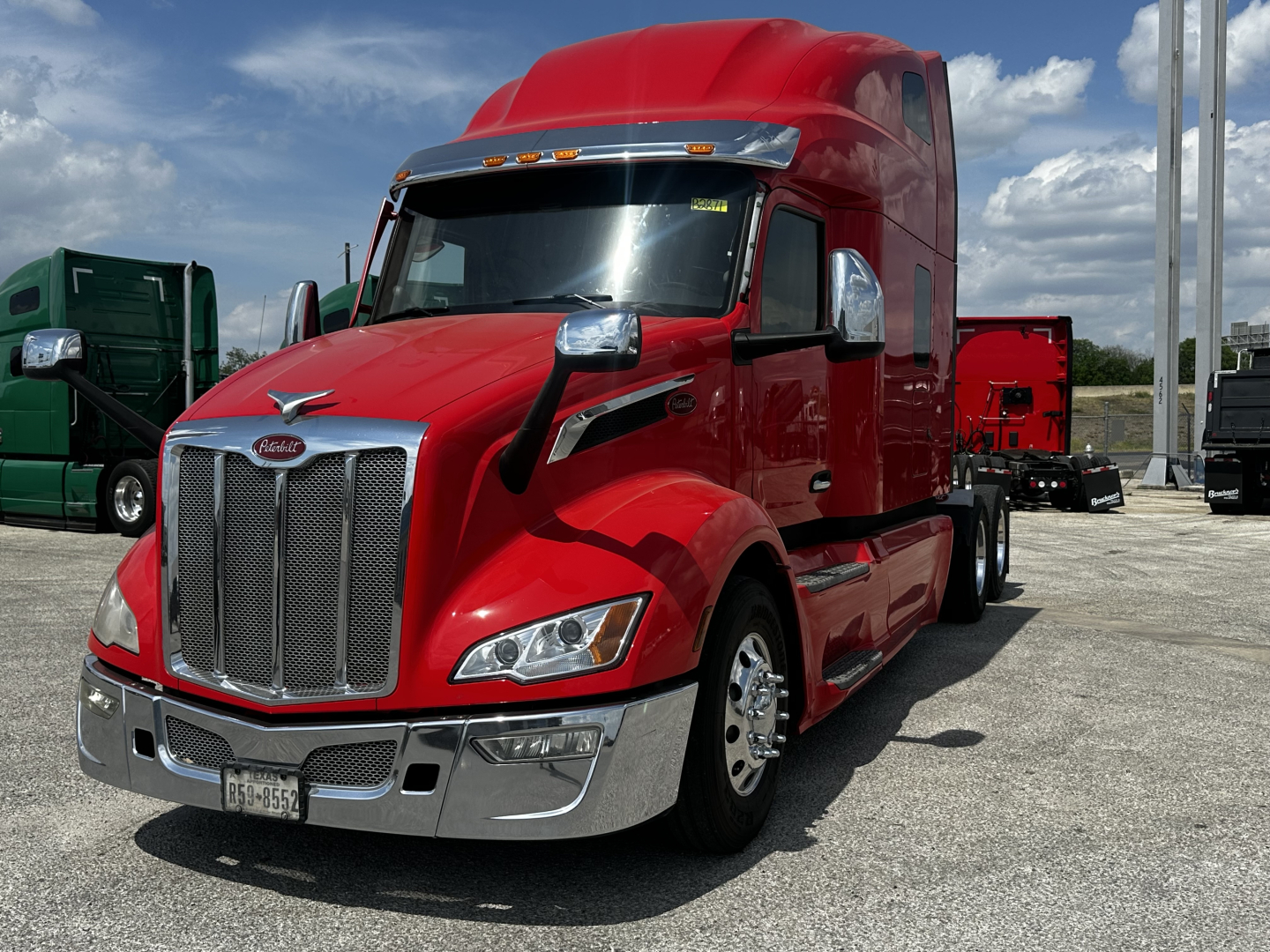 Peterbilt 579 red semi-truck in a lot, front three-quarter view showing chrome grille, dual headlights, and aerodynamic sleeper cab.