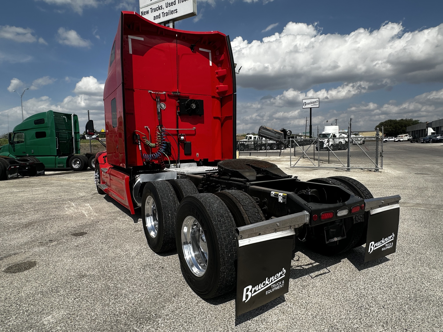 Peterbilt 579 sleeper tractor rear view showing dual rear axles, red cab, fifth wheel, and mud flaps with Buckeye logo in a truck yard.