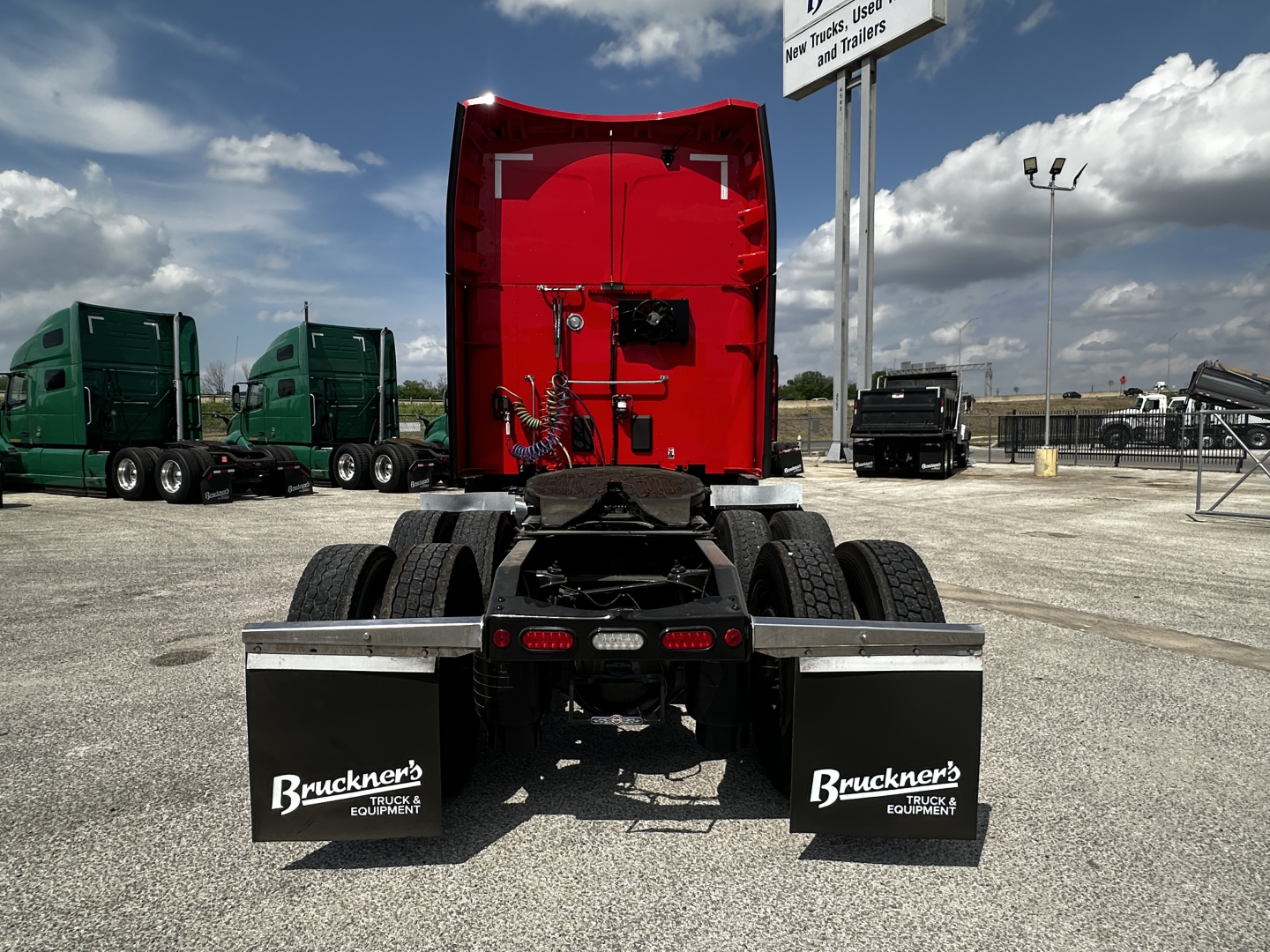 Peterbilt 579 rear view showing fifth wheel and dual rear mud flaps with Bruckner’s Truck Equipment branding, red sleeper cab, highway trucks lot.