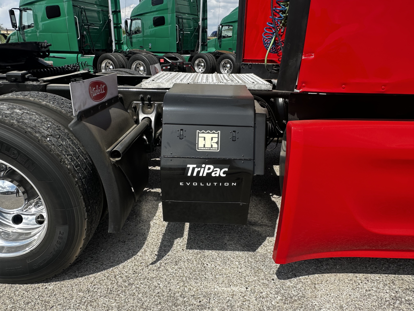 Peterbilt 579 truck side view showing TriPac Evolution battery/power unit under the cab with green trucks in background.