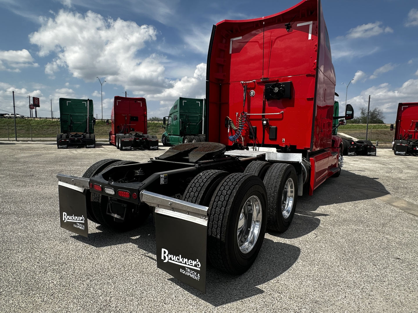 Peterbilt 579 truck tractor rear view showing red sleeper, dual rear axles, mud flaps, and fifth wheel area in a dealership lot.