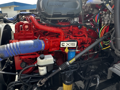 Peterbilt 579 engine bay showing Cummins X15 engine with red components, blue intake hose, and various hoses and wiring harnesses.