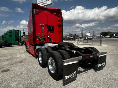 Peterbilt 579 sleeper tractor rear view showing dual rear axles, red cab, fifth wheel, and mud flaps with Buckeye logo in a truck yard.