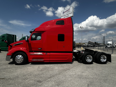Red Peterbilt 579 tractor truck side view in a dealership lot with sleeper cab and chrome wheels.