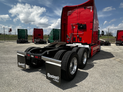 Peterbilt 579 truck tractor rear and sleeper with red cab, black fenders, dual rear axles, mud flaps, and chassis adapters; visible VIN and stock number field text not legible; overcast sky.