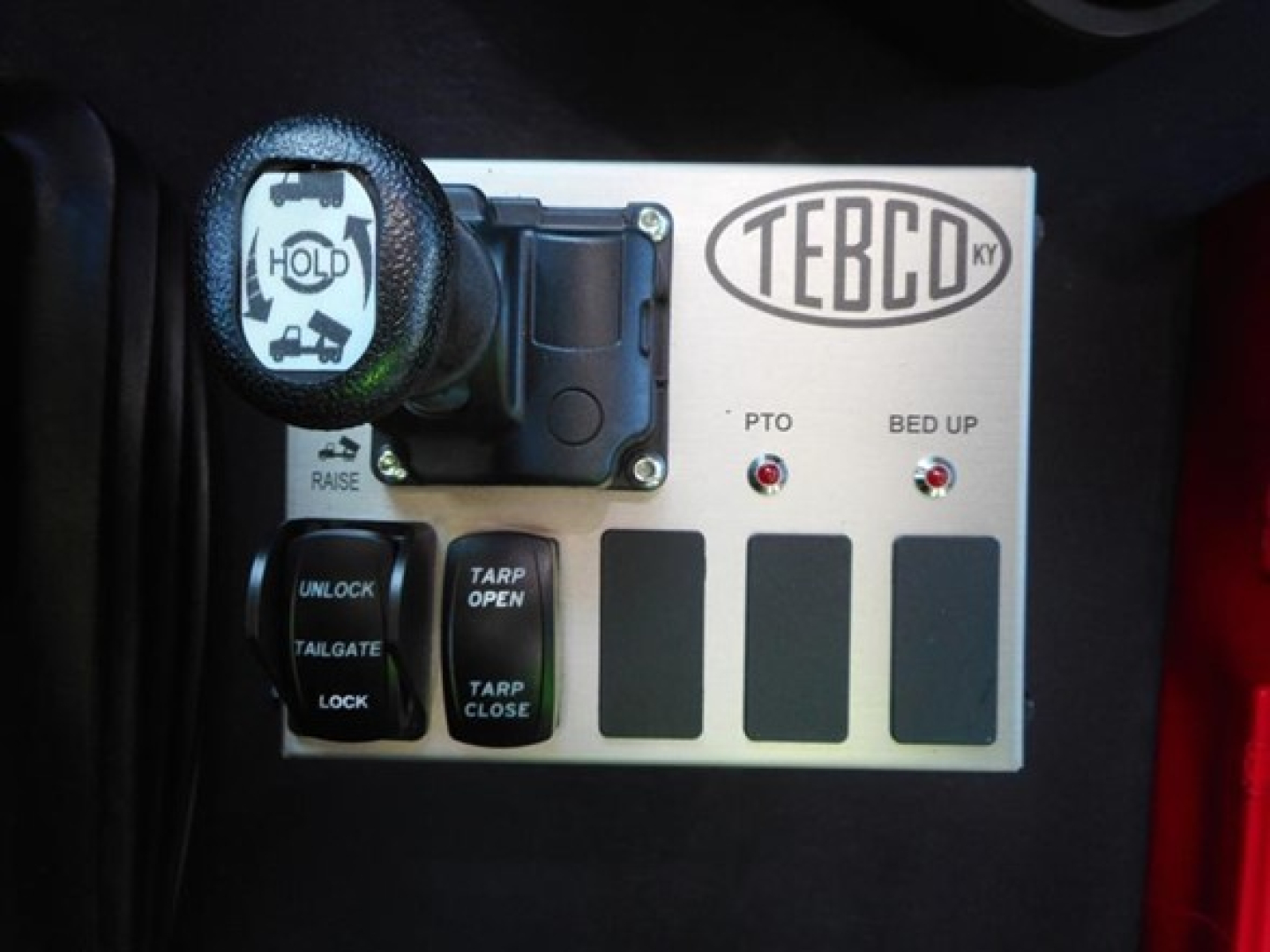 TEBCO control panel with hold strap, PTO and bed up indicators, and toggle switches in truck cab.