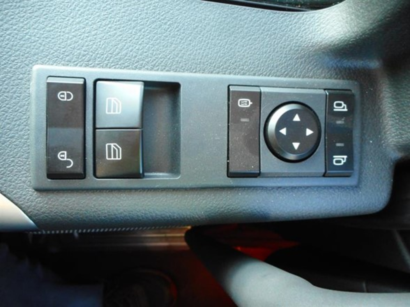 Control panel with window and mirror adjustment switches in a truck cab; visible icons include window controls, mirror adjustment pad, and circular directional pad.