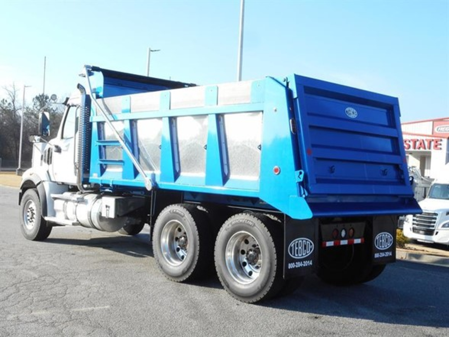Blue dump bed of a 2026 Western Star 47X in a parking lot, rear and side view showing dump body and dual rear axles.