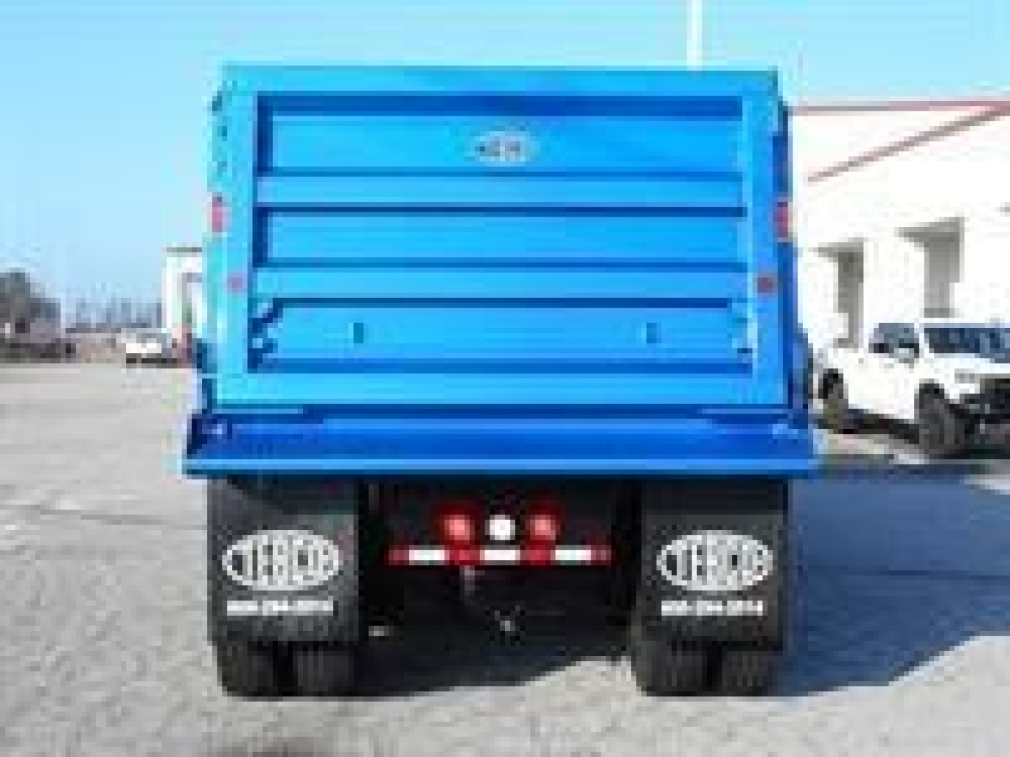 Trailer/back of a blue dump truck bed showing rear wheels with FOLDABLE mudflaps and taillights.