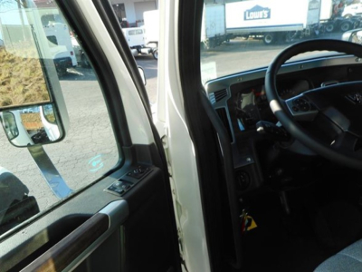 Truck interior dash and steering wheel visible through open door; exterior side mirror and dealership lot reflections in window.
