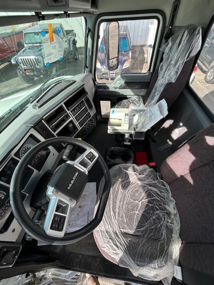 Truck cockpit interior showing steering wheel, driver's seat wrapped in plastic, dashboard with instrument cluster, and auxiliary controls in cabin.