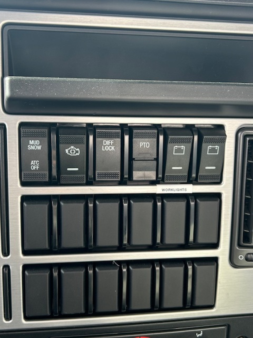 Dashboard switches and controls on a new Mack MD7 truck showing multiple labeled buttons such as MUD/SNOW, DIFF LOCK, PTO, and ATC OFF.