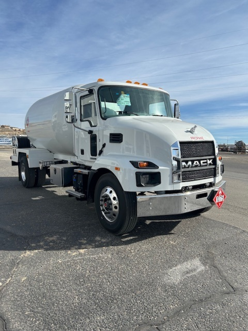 Mack MD7 tanker truck in a parking lot, front three-quarter view, white cab with chrome bumper, orange marker lights, and a diamond placard on the front.